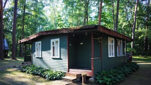 A small, single-story cabin with a porch, surrounded by a forest. - Asmonai Campsite (Kintai)