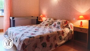 Un dormitori amb un llit, dues taules de nit amb làmpades, una finestra amb cortines i una làmpada de paret.