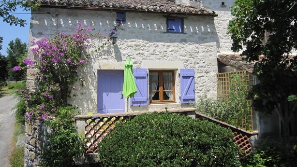 Una casa de pedra amb teulada de rajola, una porta de fusta i un petit balcó amb un para-sol verd.