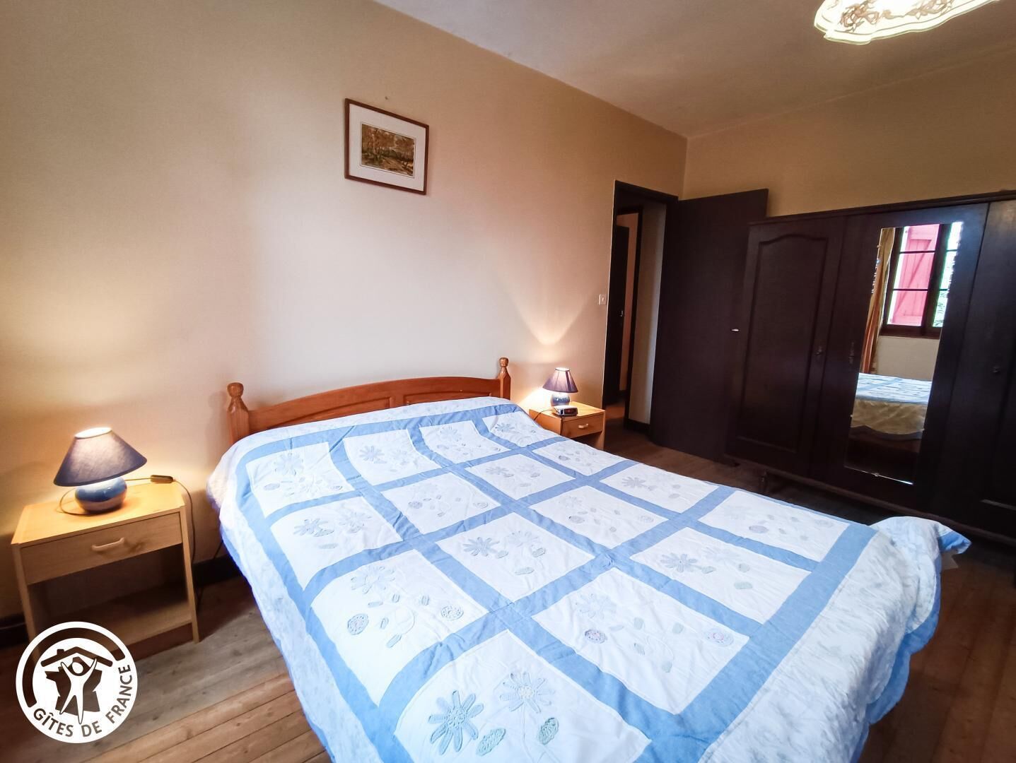 A bedroom with a wooden bed, two bedside tables with lamps, a wardrobe, and a framed picture on the wall.