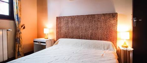 Habitación de hotel con una cama grande, dos mesitas de noche con lámparas, un cuadro enmarcado en la pared y una ventana con cortinas.