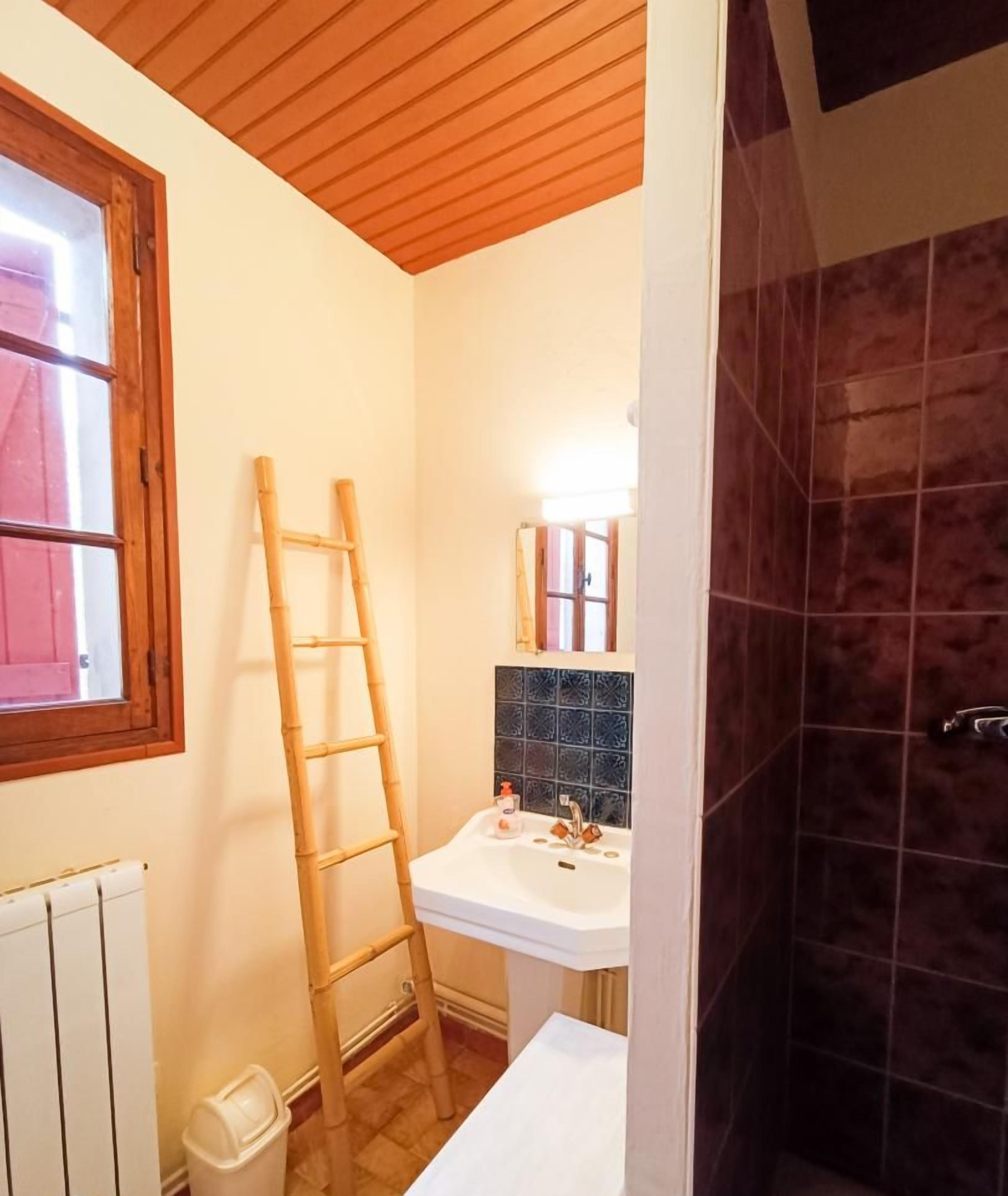 A bathroom with a wooden ladder leaning against the wall, a white sink with a mirror above it, and a shower area with dark tiles.