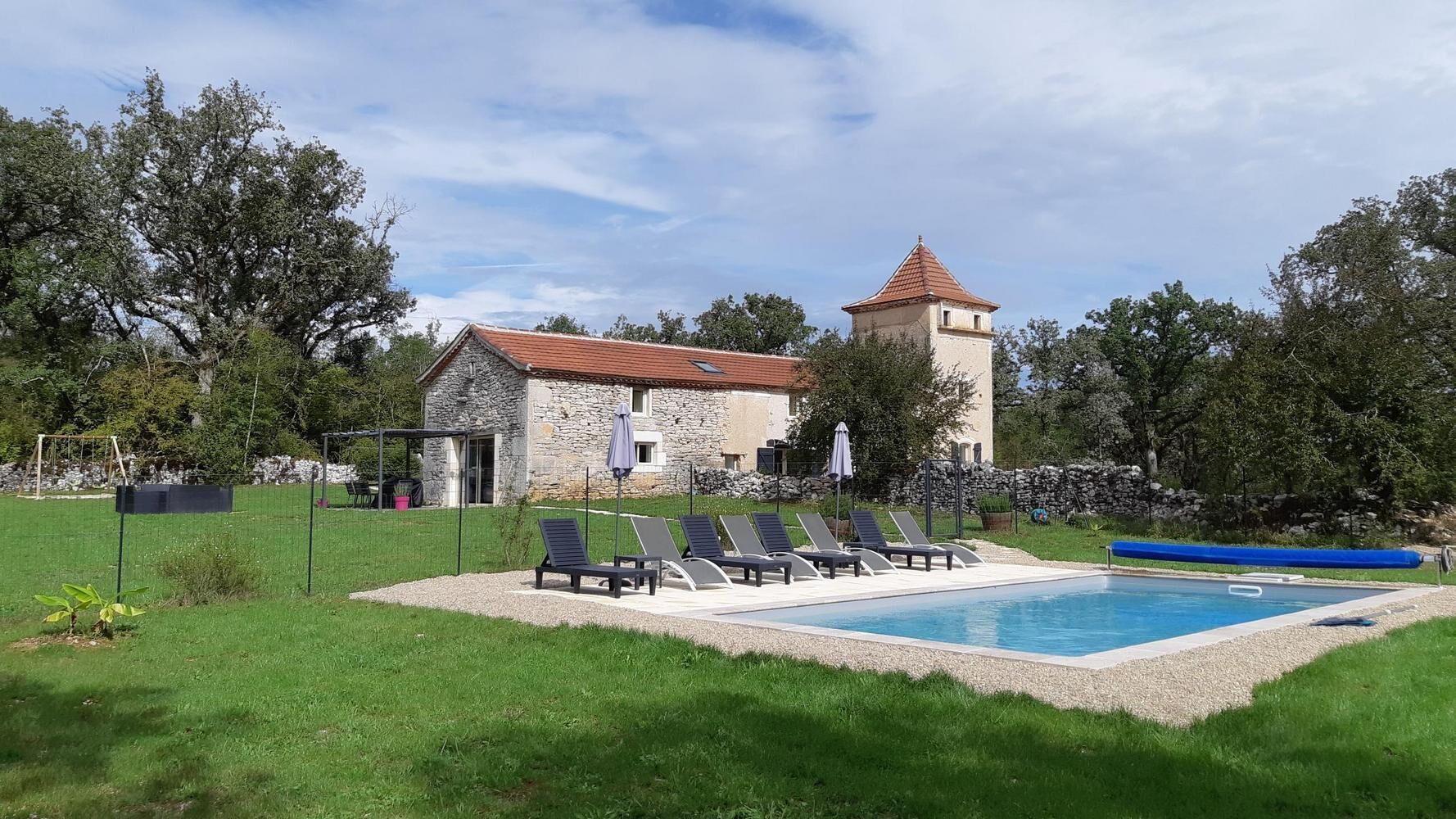 A stone building with a tower, a swimming pool, and lounge chairs.