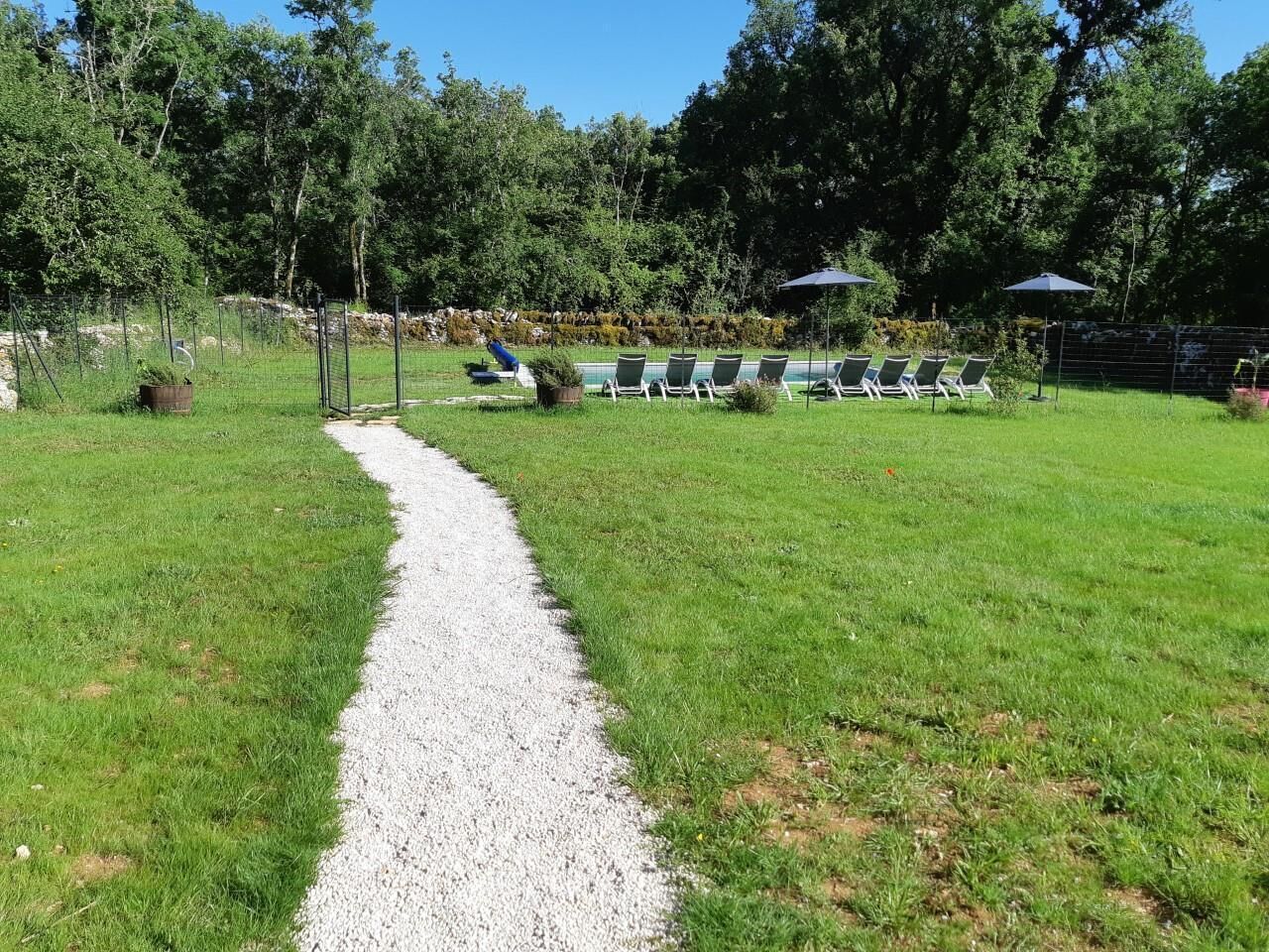 A gravel path leading to a pool area with lounge chairs and umbrellas.