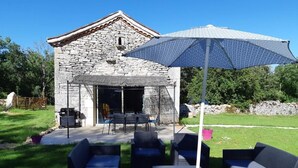 Ein Steinhaus mit einer überdachten Terrasse, die Gartenmöbel und einen Sonnenschirm hat.