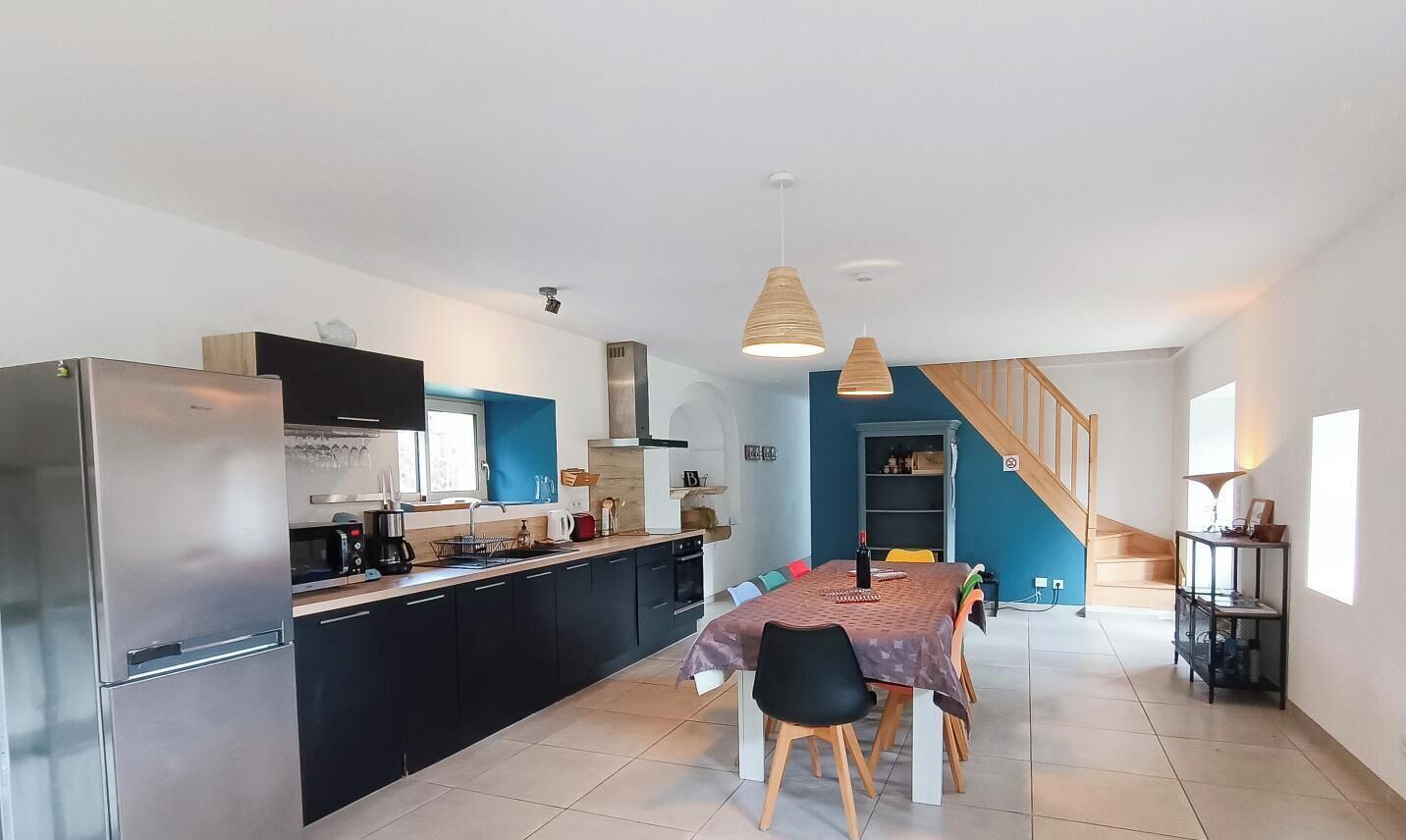 Una cocina moderna con un refrigerador empotrado, un comedor con mesa y sillas, y una escalera que sube a otro nivel.
