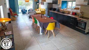 Eine moderne Küche mit Essbereich, inklusive großer Kochinsel, integrierter Geräte und Ausblick ins Freie.