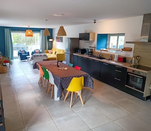A modern kitchen with a dining area, featuring a large island, built-in appliances, and a view to the outside.