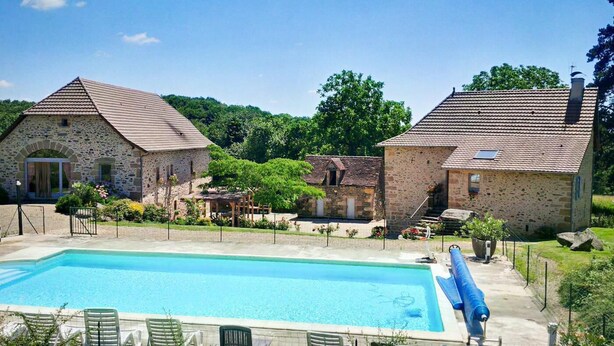 Un edificio in pietra con piscina, immerso nel verde e sotto un cielo sereno.