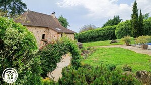 Una casa in pietra con tetto in tegole, circondata da rigogliosa vegetazione e un giardino curato.