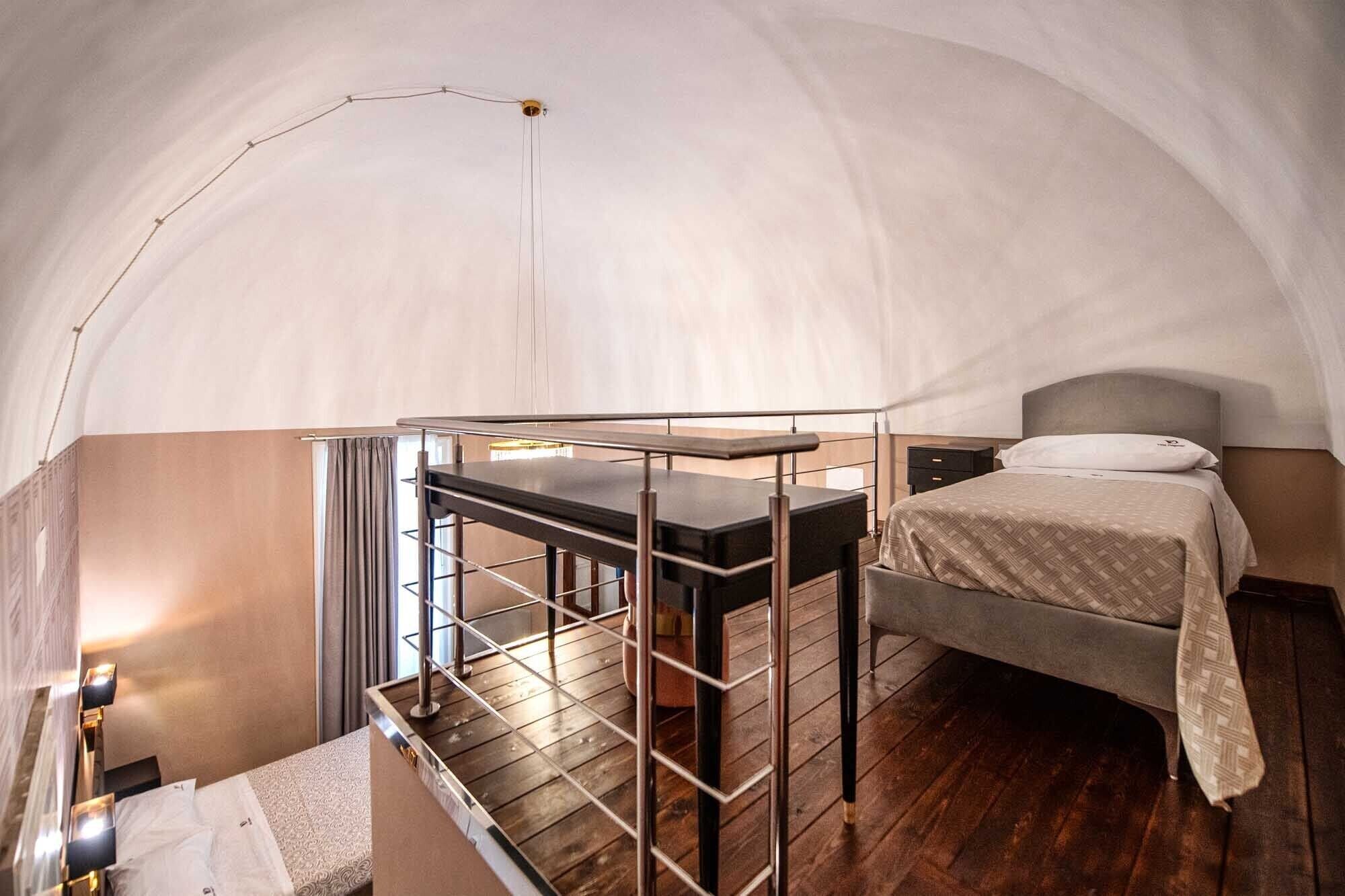 A compact, well-lit tent-style room with a bed, a small desk with a chair, and a staircase leading to an upper level.