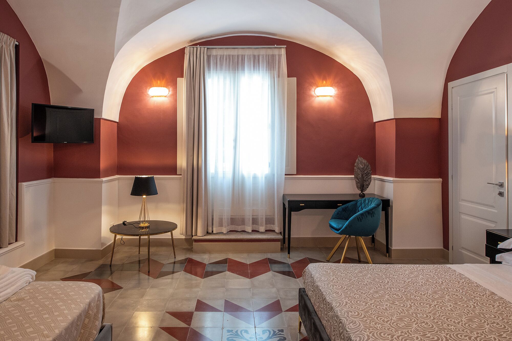 Quarto de hotel com cama, escrivaninha, cadeira, televisão e janela com cortinas.