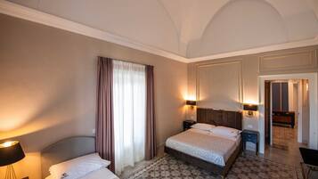 Une chambre d’hôtel comprenant un lit, une table de chevet, une lampe, une fenêtre avec des rideaux et un luminaire fixé au mur.