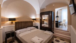 Habitación de hotel con una cama grande, dos mesitas de noche, un espejo y un televisor montado en la pared.
