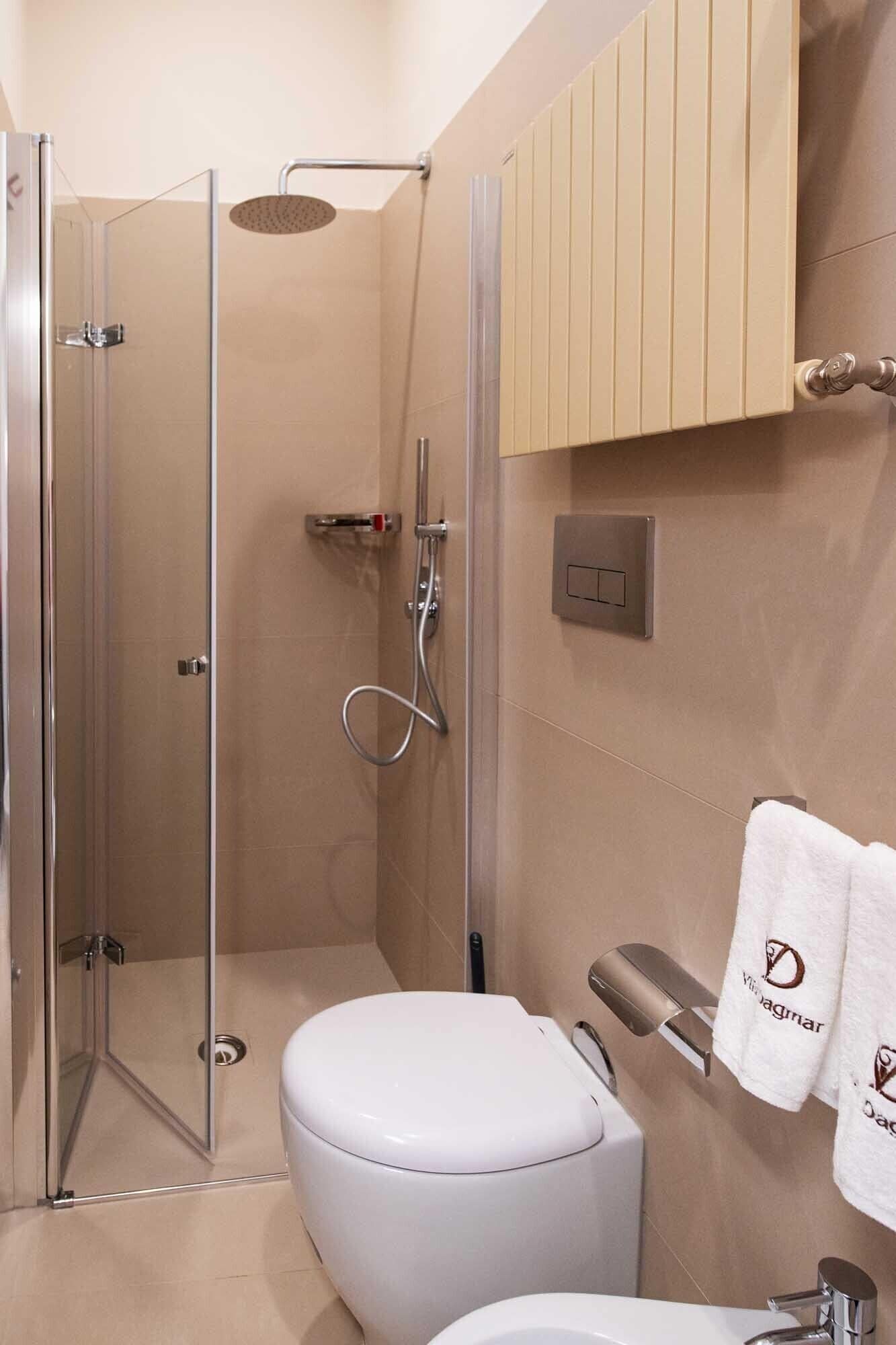 Un baño moderno con ducha envuelta en vidrio, inodoro blanco y tocador de madera con toallero.