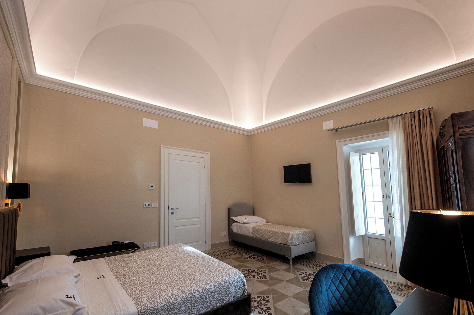 Ein Hotelzimmer mit Bett, Sessel, Fernseher und einer Tür zu einem Balkon.