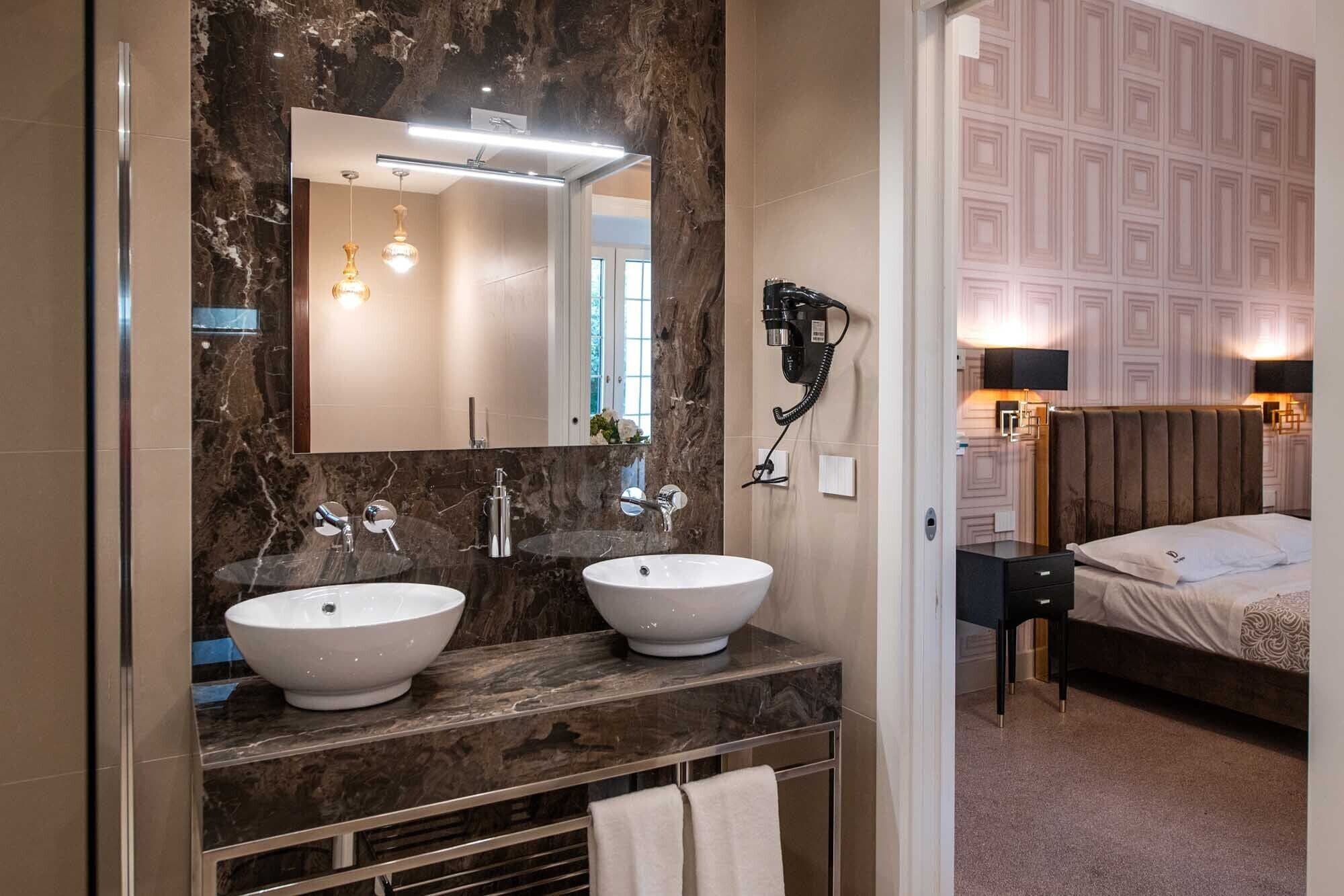 A modern bathroom with two sinks, a large mirror, and a hairdryer mounted on the wall.
