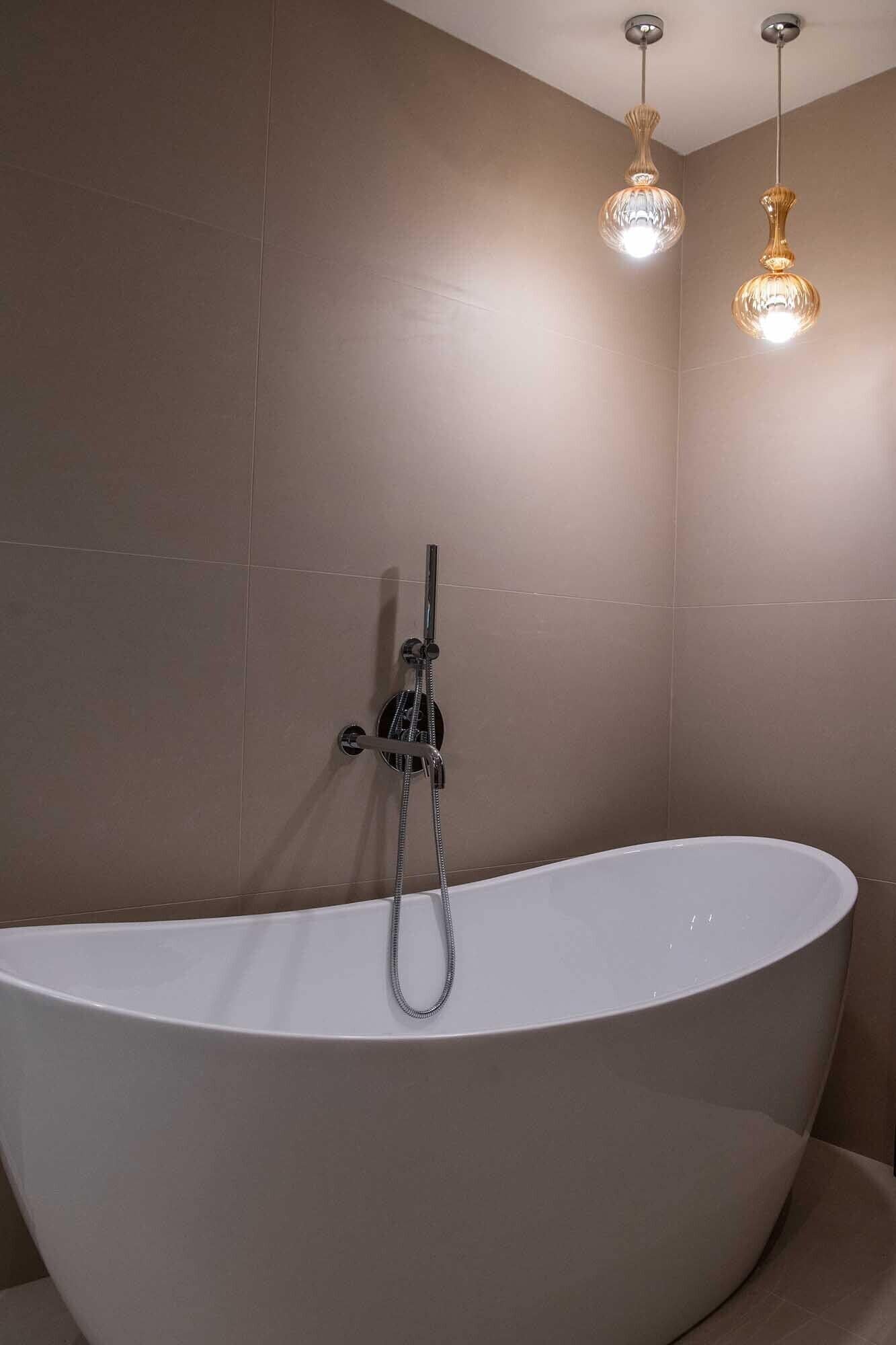 A modern bathroom with a freestanding bathtub, a handheld showerhead, and two pendant lights.