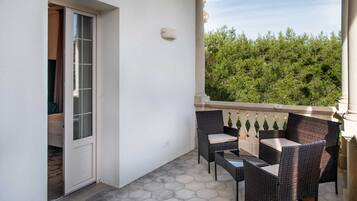 Ein Balkon mit Korbmöbeln, einer Glastür und Blick auf Grünflächen.