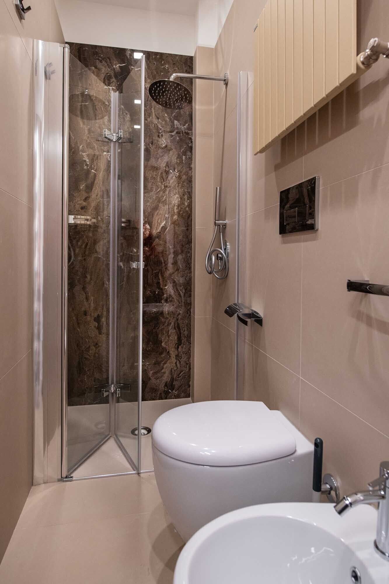 Un baño moderno con ducha de vidrio, inodoro blanco y lavamanos con espejo.