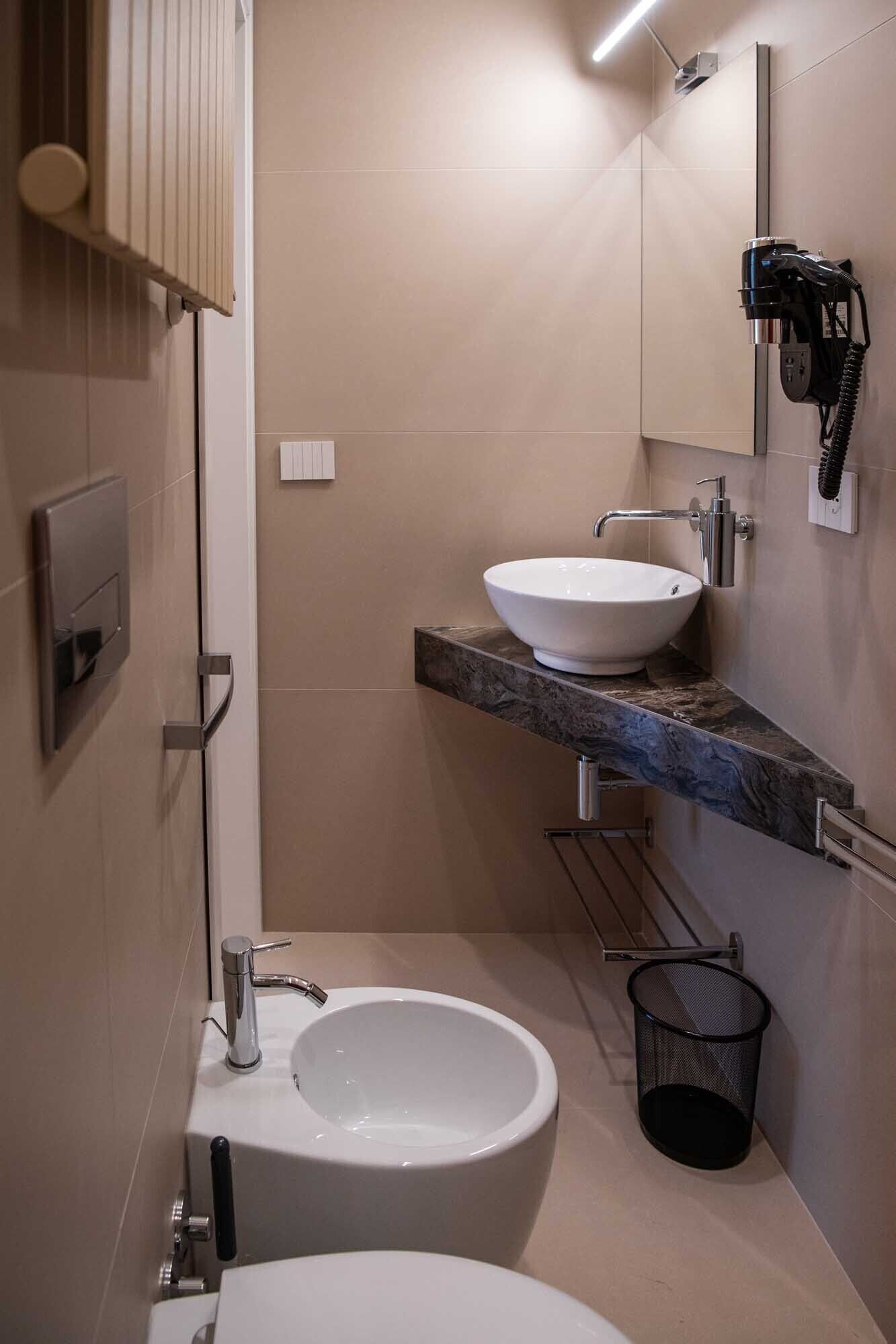 A modern bathroom with a white toilet, a white sink with a marble countertop, and a shower area.