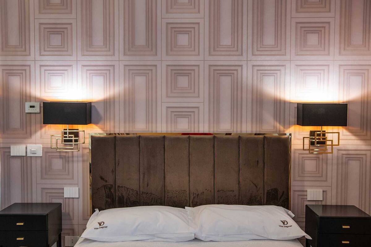 Ein Hotelzimmer mit einem hölzernen Kopfteil, zwei Nachttischen, einem Bett mit weißer Bettwäsche und zwei Wandlampen.