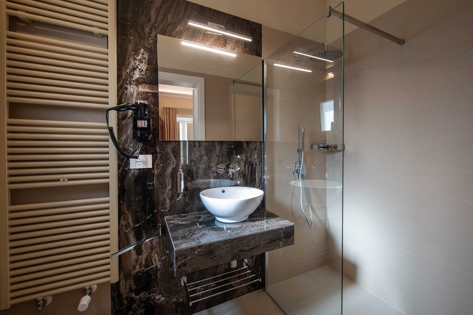 Une salle de bain moderne avec un grand miroir, un lavabo sur colonne blanc et une douche à parois de verre.