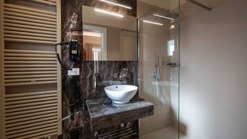 Une salle de bain moderne avec un grand miroir, un lavabo sur colonne blanc et une douche à parois de verre.