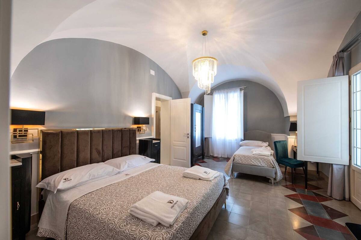 Ein Hotelzimmer mit zwei Betten, einer Kristallleuchter, einem Fernseher und Blick auf die Stadt.