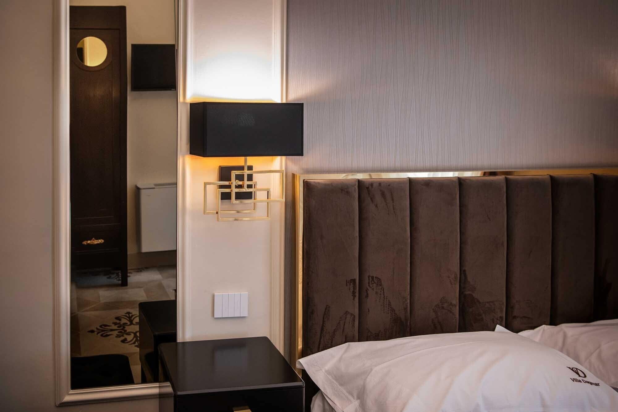 A hotel room with a bed, a nightstand, a wall-mounted lamp, and a mirror.