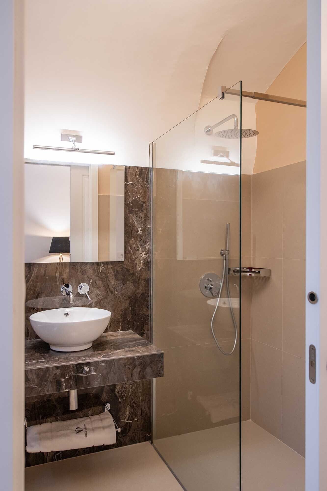 A modern bathroom with a glass-enclosed shower, a marble sink, and a mirror above the sink.