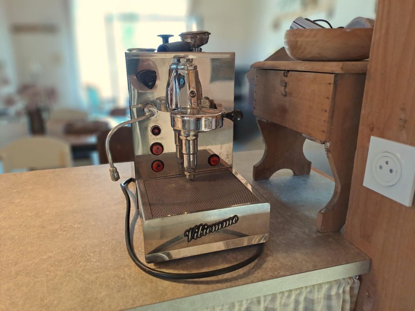 Eine alte Espressomaschine auf einer Küchenarbeitsplatte, im Hintergrund ein Holzschrank.