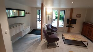 Un salon comprenant un canapé, deux fauteuils, une table basse, un téléviseur et une porte-fenêtre coulissante donnant sur l’extérieur.