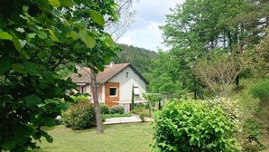 Une maison avec un jardin, une terrasse en bois et une colline en arrière-plan.