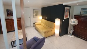 Un salon avec un canapé jaune, un fauteuil violet, un lampadaire et une lampe de sol, ainsi qu  ’un meuble en bois.