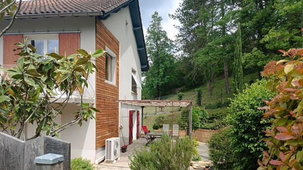 Une maison dotée d’un patio couvert, d’un jardin avec différentes espèces de plantes et d’un chemin en pierre.