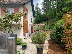 Una casa con un porche cubierto, un jardín con diversas plantas y un camino de piedra.