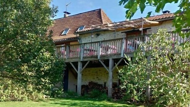 Una casa con balcón, rodeada de césped cuidado y árboles.