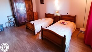 Ein Zimmer mit zwei Holzbetten, einem Holzschrank, einem Stuhl, einem kleinen Tisch mit einer Lampe und einem Bild an der Wand.