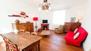 Ein Wohnzimmer mit Esstisch aus Holz, Stühlen, einem roten Sofa, einem Fernseher und einem Kamin.