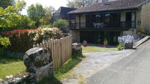 A traditional stone building with a wooden balcony, surrounded by a garden with red flowers and a wooden fence. - Gîtes de France® - La Grange de Marie (RUDELLE)
