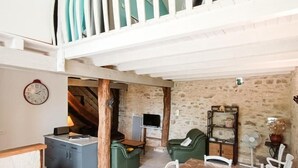 Ein großzügiger Essbereich mit langem Tisch und Stühlen, eine Sitzecke mit Sofa und Sesseln sowie ein Balkon mit Vorhängen.