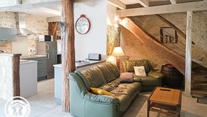 Ein gemütlicher Loftsitzbereich mit freiliegenden Holzbalken, einem grünen Ledersofa, einem Holztisch und einer Küchenzeile mit modernen Geräten.