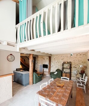 A spacious dining area with a long table and chairs, a seating area with a sofa and chairs, and a balcony with curtains. - Gîtes de France® - La Grangette de Laval (LALBENQUE)