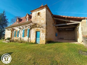 A stone house with a red-tiled roof, a blue door, and a covered porch area.