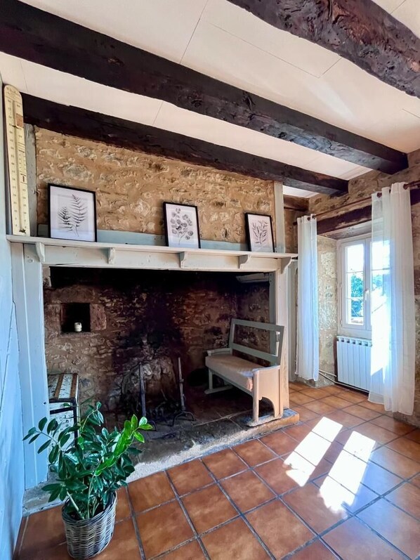 A rustic room with a stone fireplace, wooden beams, and a tiled floor.