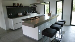 Una cocina moderna con una isla central, taburetes de bar y un amplio ventanal que proporciona luz natural.