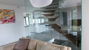 Una sala de estar moderna con una escalera de cristal, un sofá beige y un cuadro abstracto colorido en la pared.