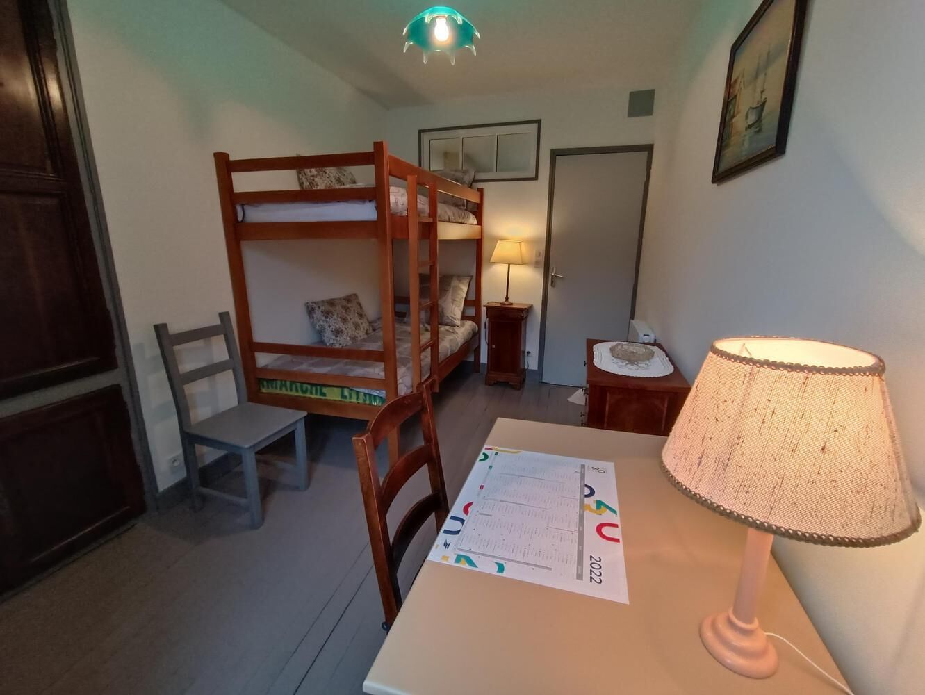 Una habitación con una cama nido, un escritorio con lámpara, una silla y una pequeña mesa con lámpara.