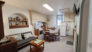 Un espai vital compacte amb sofà, taula de centre, taula de menjador i cadires. Es veu una zona de cuina amb fogó, forn i nevera.